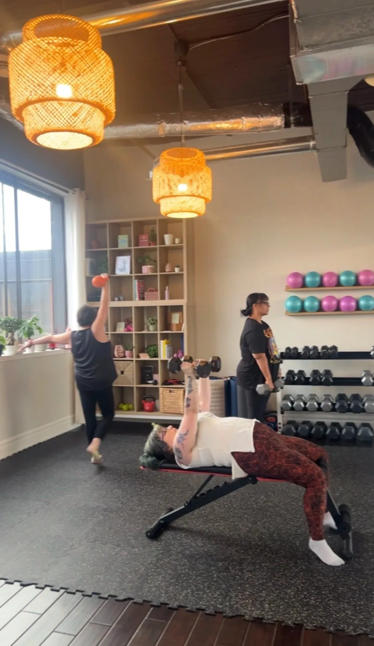 Members working through a functional strength exercise with dumbbells at the studio, with the dumbbell rack and exercise balls along the wall