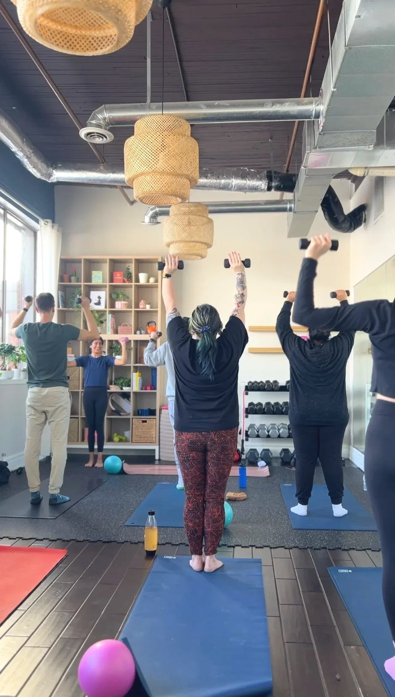 Group functional strength class raising dumbbells overhead at the studio