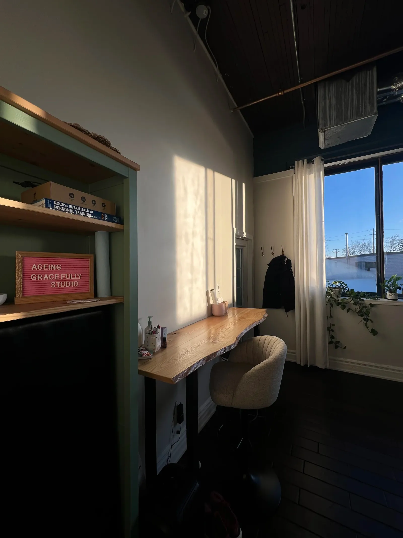 Desk and seating nook inside the studio, with a sign reading "Ageing Gracefully Studio" on the shelf