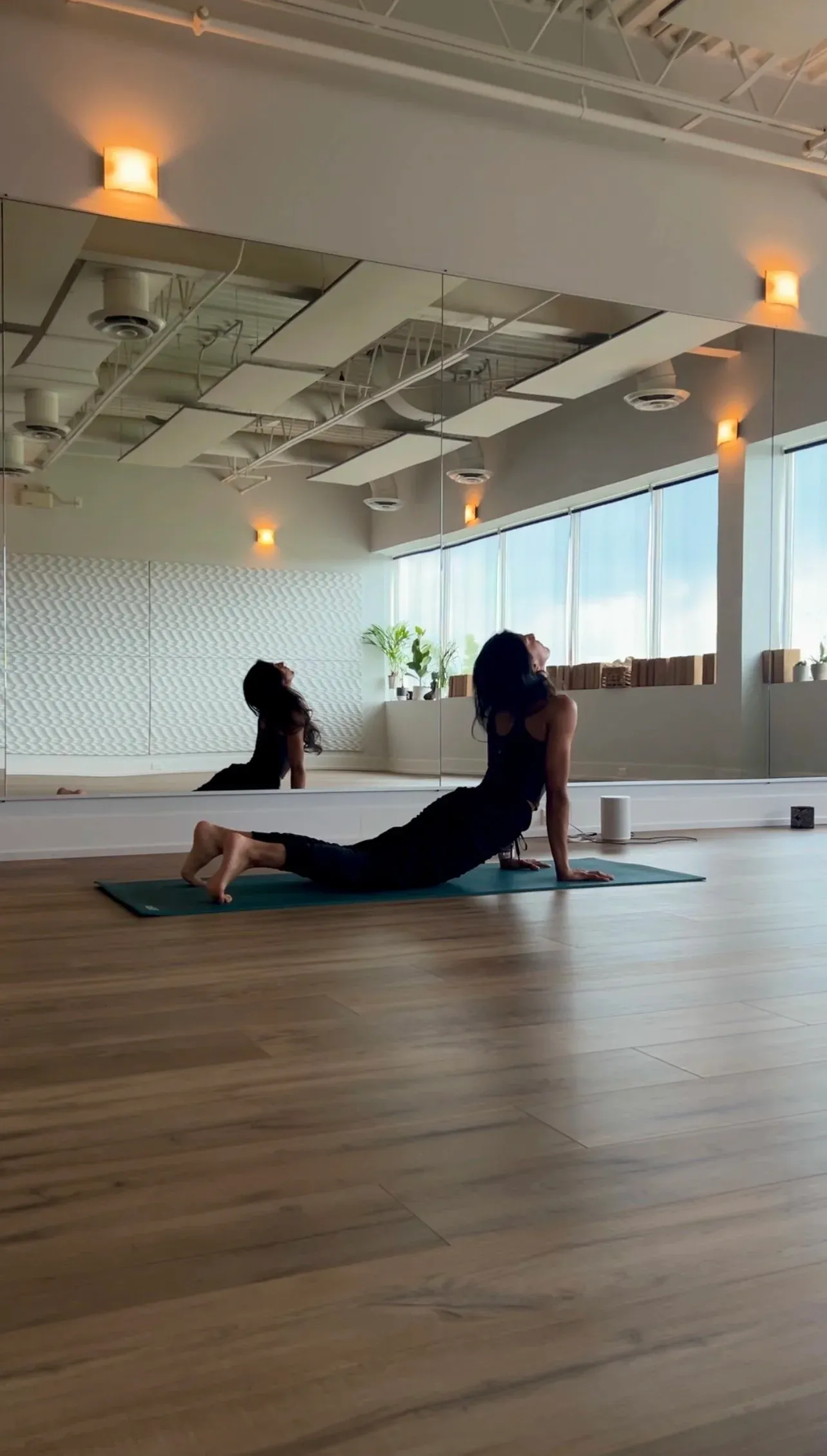 Woman in an upward-facing stretch on a yoga mat in a bright, mirrored studio room